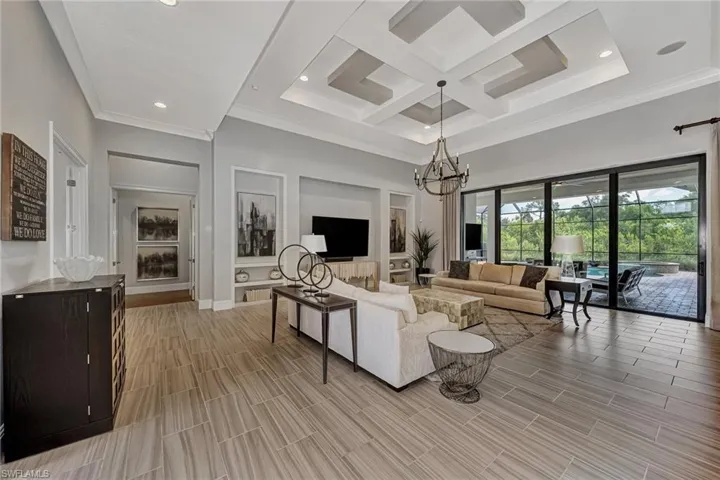 Living room featuring crown molding, beamed ceiling, coffered ceiling, a towering ceiling, and a chandelier