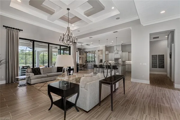 Living room featuring a notable chandelier, plenty of natural light, coffered ceiling, and crown molding