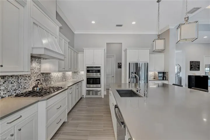 Kitchen with stainless steel appliances, sink, white cabinetry, and backsplash