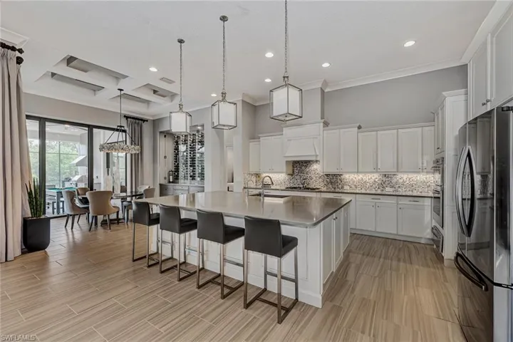 Kitchen featuring coffered ceiling, stainless steel appliances, tasteful backsplash, an island with sink, and pendant lighting