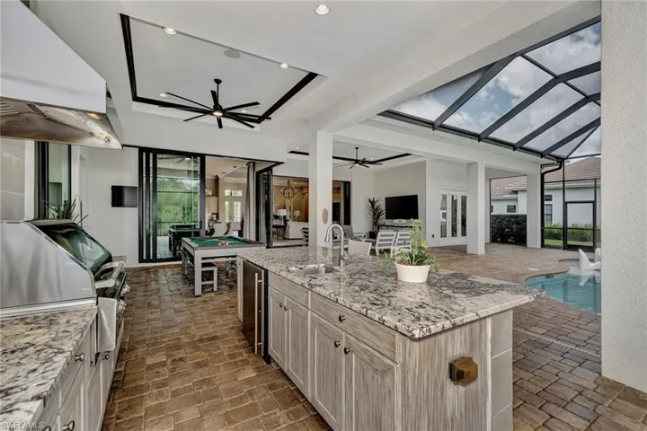 outdoor Kitchen featuring light stone counters, ceiling fan, a kitchen island with sink, custom exhaust hood, and sink