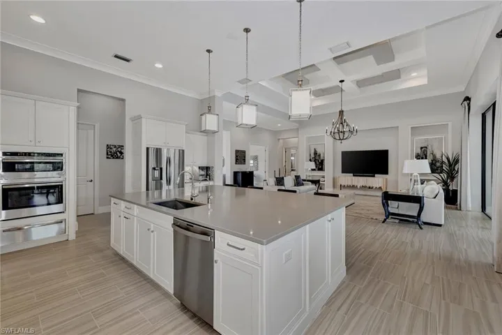 Kitchen featuring an island with sink, coffered ceiling, sink, white cabinetry, and appliances with stainless steel finishes