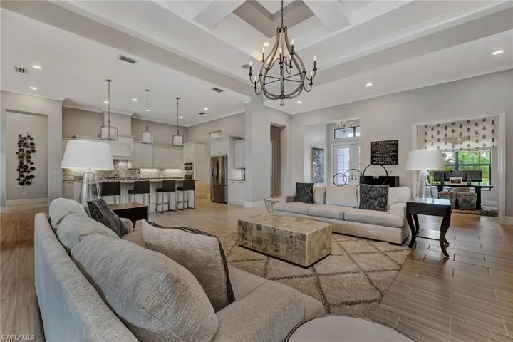 Living room with beamed ceiling, crown molding, coffered ceiling, and an inviting chandelier
