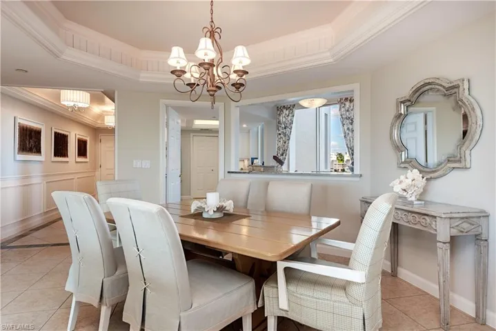 Dining area with a tray ceiling, a notable chandelier, light tile patterned flooring, and crown molding
