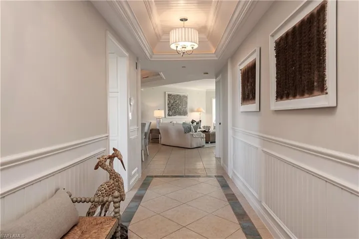 Hallway with ornamental molding, light tile patterned floors, and a tray ceiling