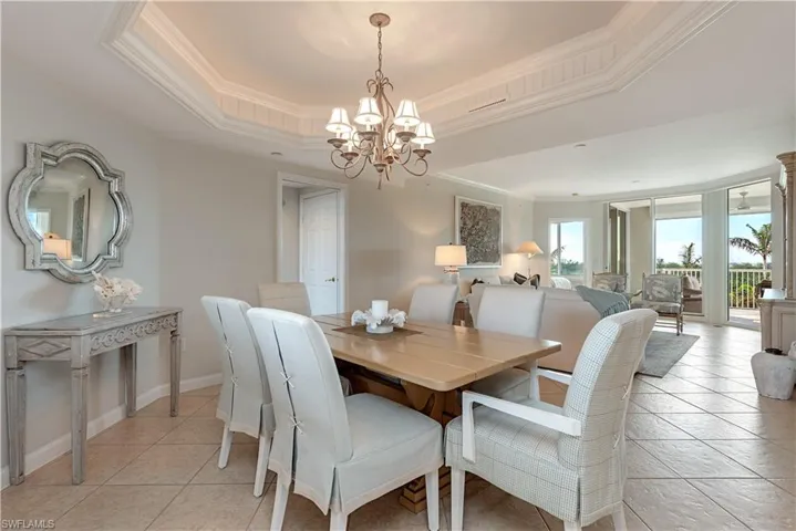 Dining area with light tile patterned floors, a chandelier, a raised ceiling, and crown molding