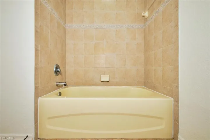Full bath with washtub / shower combination and a textured wall