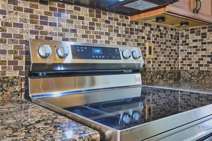 Detailed view of backsplash, stainless steel range with electric cooktop, and dark stone countertops
