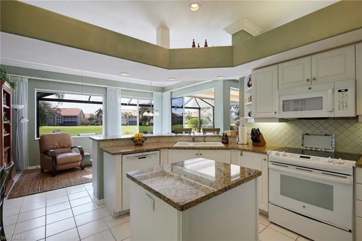 Kitchen featuring granite countertops, white appliances, a kitchen island, and white cabinetry...windows and sliders galore for an abundance of natural light!