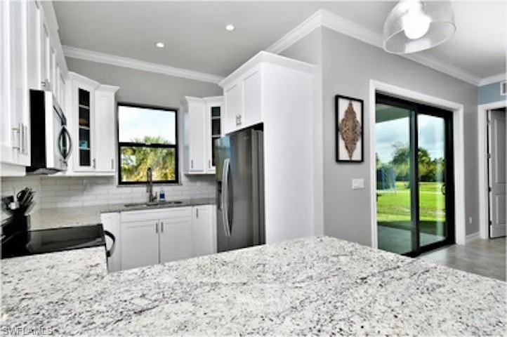 Kitchen featuring ornamental molding, decorative backsplash, light stone countertops, stainless steel appliances, and white cabinets