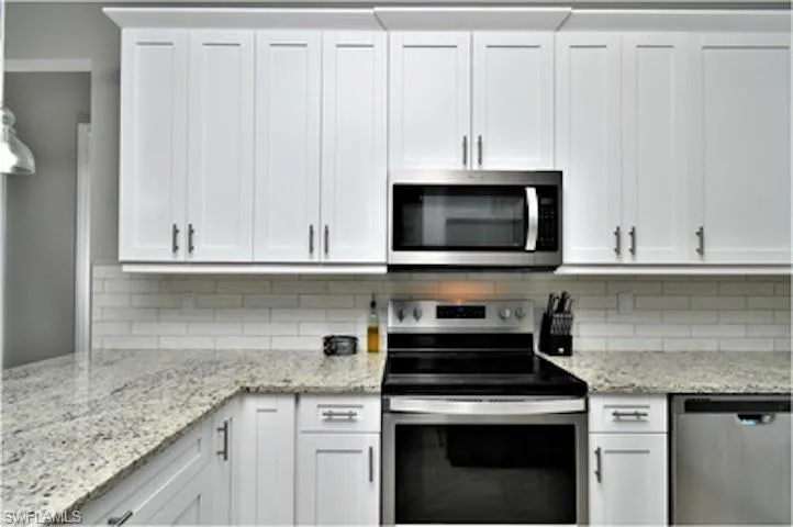 Kitchen featuring stainless steel appliances, white cabinetry, and light stone counters
