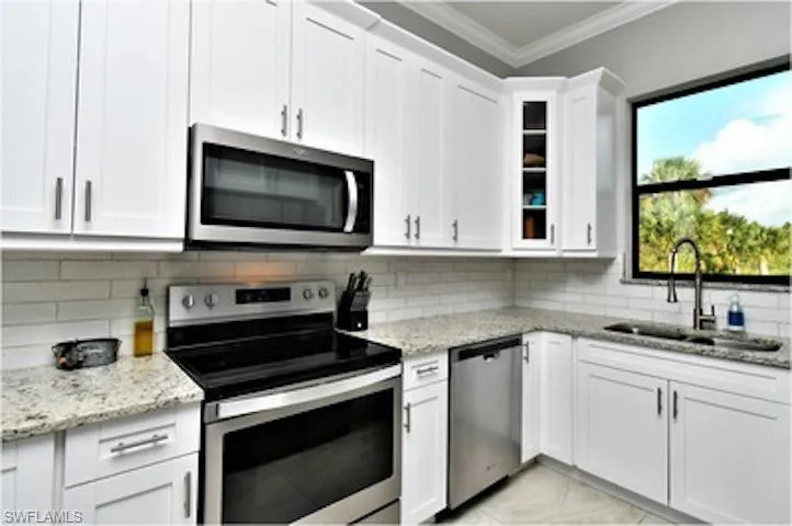 Kitchen featuring stainless steel appliances, glass insert cabinets, ornamental molding, light stone counters, and white cabinets