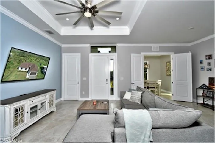 Living room with ceiling fan, a tray ceiling, crown molding, and recessed lighting