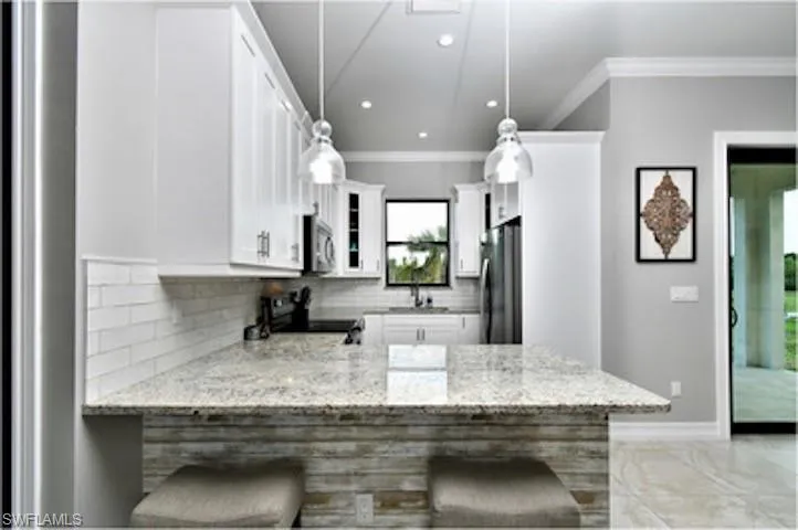 Kitchen with light stone countertops, a peninsula, recessed lighting, crown molding, and tasteful backsplash