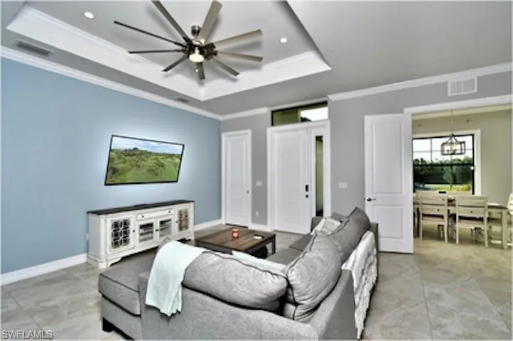 Living room with a tray ceiling, crown molding, a ceiling fan, a chandelier, and recessed lighting