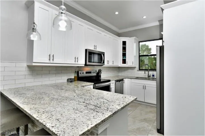 Kitchen featuring a peninsula, white cabinets, stainless steel appliances, light stone counters, and ornamental molding