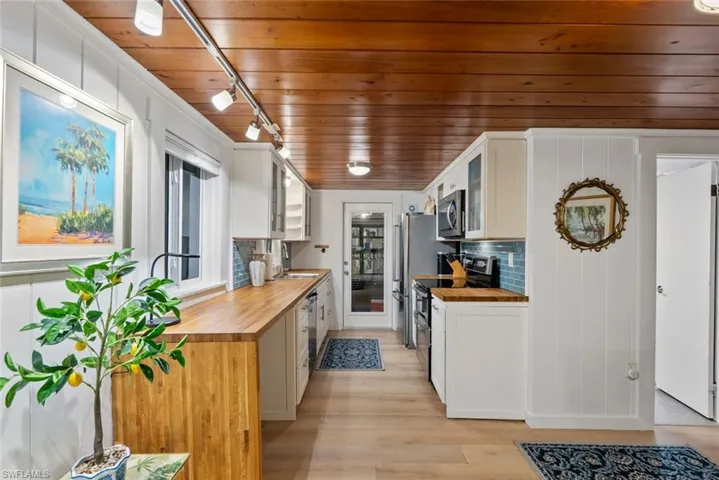 Kitchen with wooden ceiling, white cabinetry, stainless steel appliances, wooden counters, and light wood-style floors