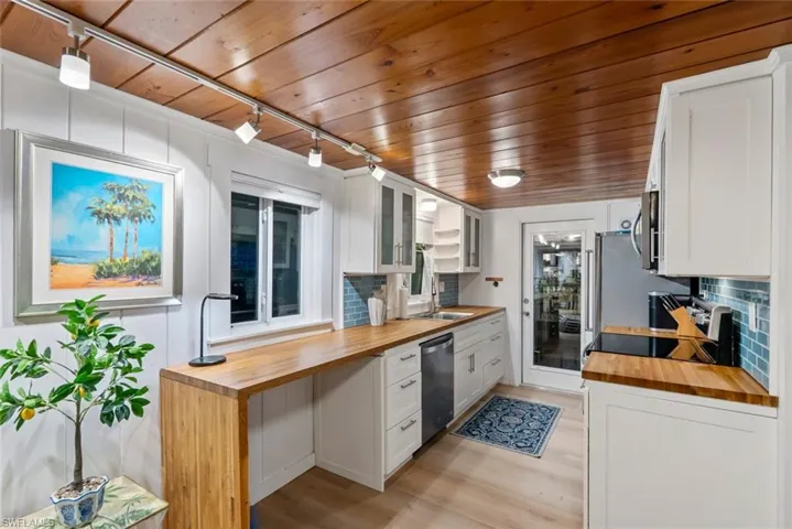 Kitchen with butcher block counters, white cabinetry, wood ceiling, track lighting, and glass insert cabinets