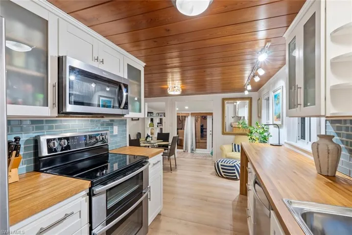 Kitchen with glass insert cabinets, appliances with stainless steel finishes, white cabinetry, and wood ceiling