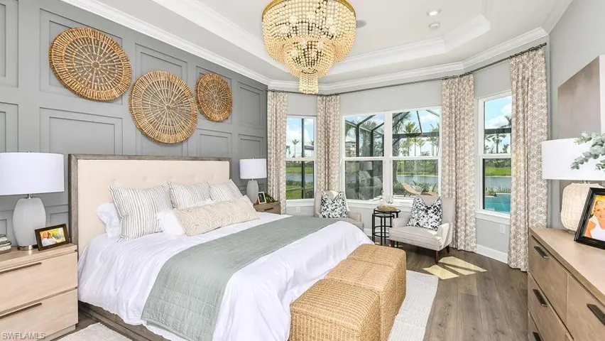 Bedroom featuring a decorative wall, ornamental molding, dark wood-type flooring, an inviting chandelier, and a tray ceiling