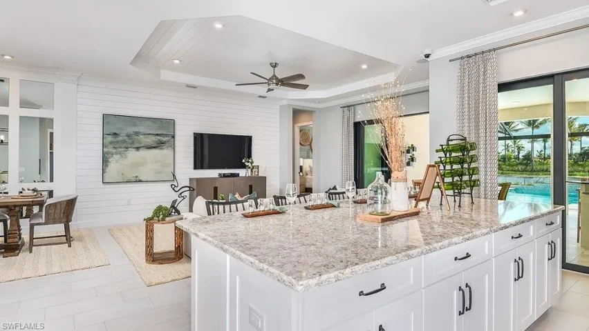 Kitchen featuring a ceiling fan, a tray ceiling, light stone counters, white cabinetry, and a kitchen island
