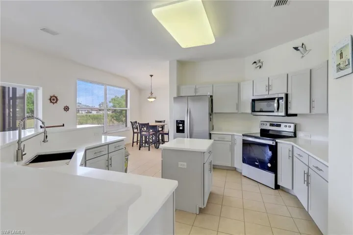 Kitchen with stainless steel appliances, a kitchen island with sink, light tile patterned flooring, light countertops, and hanging light fixtures
