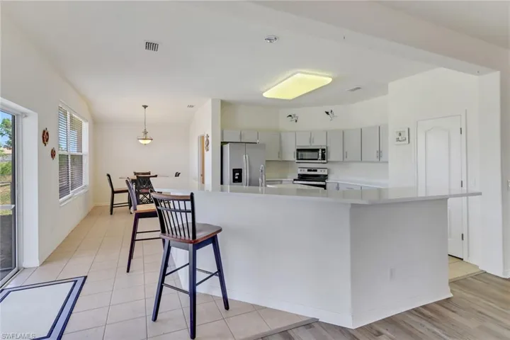 Kitchen with appliances with stainless steel finishes, light countertops, gray cabinetry, a breakfast bar area, and pendant lighting