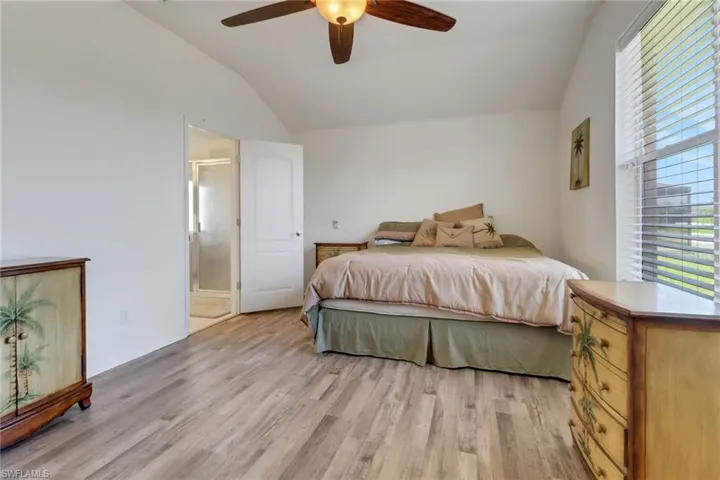 Bedroom featuring vaulted ceiling, light wood finished floors, ensuite bathroom, and ceiling fan