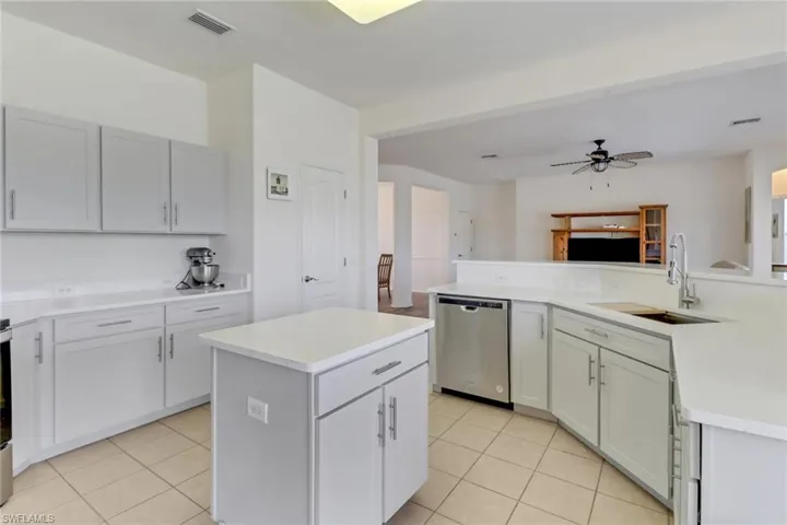 Kitchen featuring stainless steel dishwasher, light tile patterned flooring, a kitchen island, and light countertops