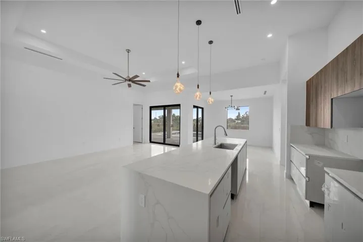 Kitchen featuring light stone countertops, modern cabinets, a center island with sink, and hanging lights