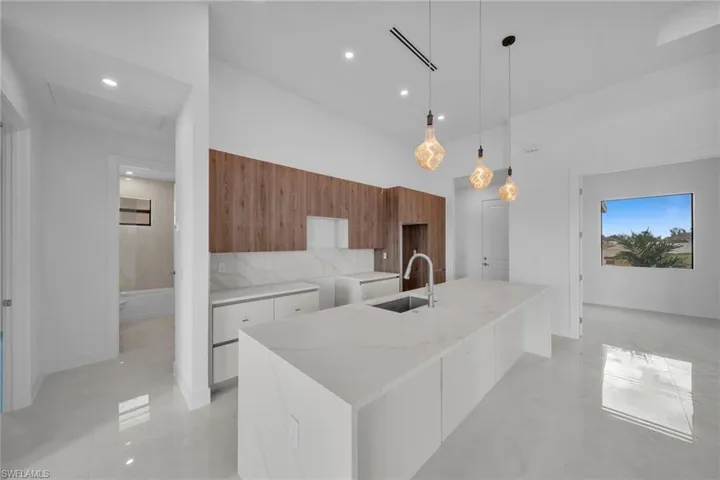 Kitchen featuring modern cabinets, light stone counters, a center island with sink, pendant lighting, and finished concrete floors