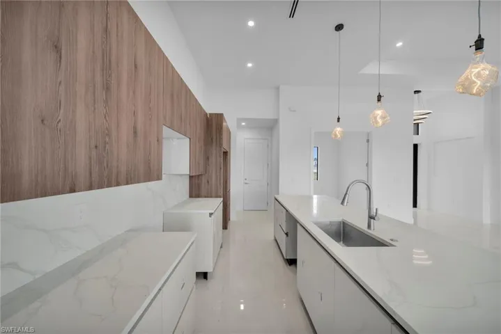 Kitchen with modern cabinets, wood finish cabinets, light stone countertops, decorative light fixtures, and wood walls