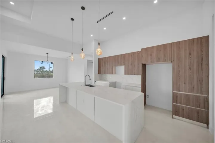 Kitchen featuring modern cabinets, light stone counters, hanging light fixtures, wood finish cabinetry, and a kitchen island with sink