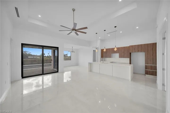 Unfurnished living room featuring a ceiling fan, a high ceiling, light marble finish flooring, and suspended lighting