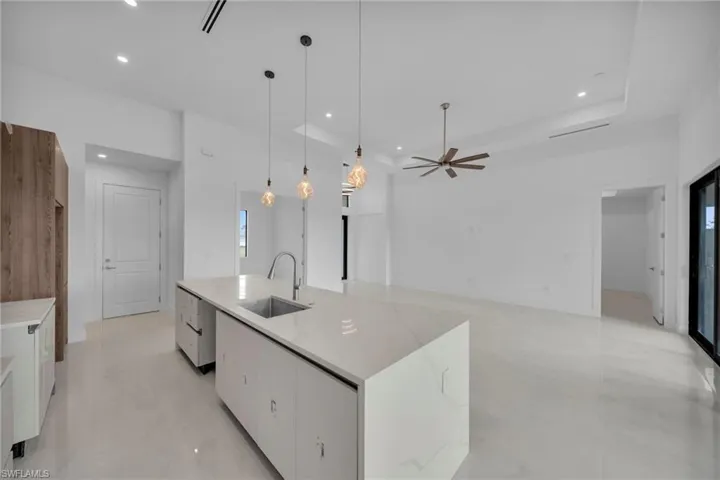 Kitchen featuring white cabinets, an island with sink, hanging light fixtures, light stone countertops, and open floor plan
