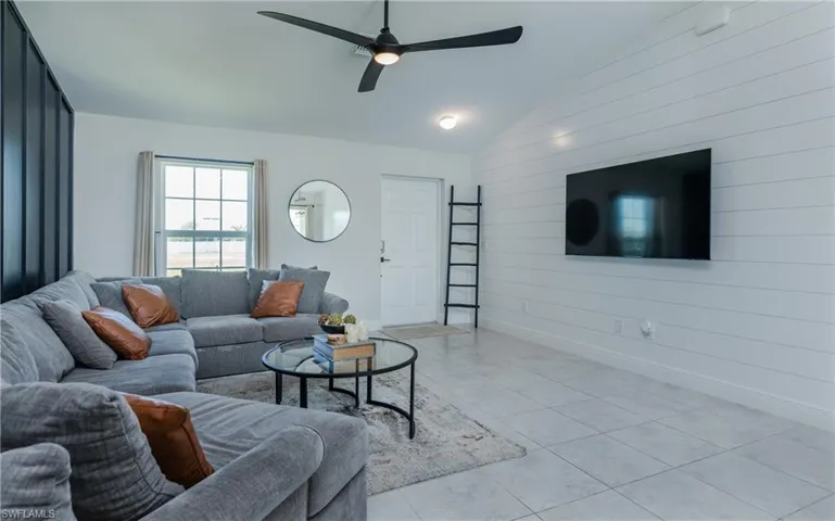 Living room with wood walls, light tile flooring, ceiling fan, and vaulted ceiling