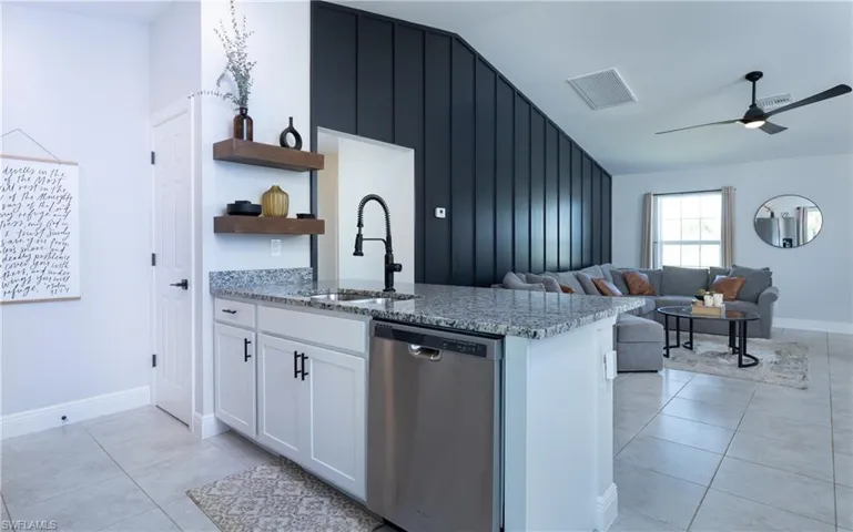 Kitchen featuring ceiling fan, stainless steel dishwasher, light tile flooring, light stone counters, and white cabinets