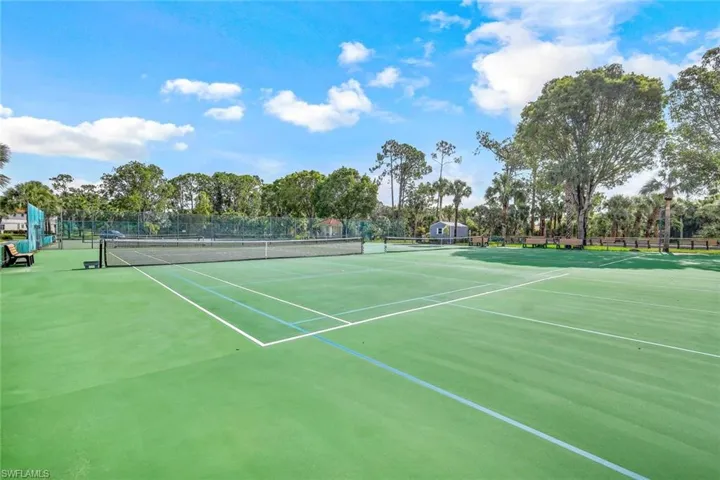 View of tennis court with view of wooded area