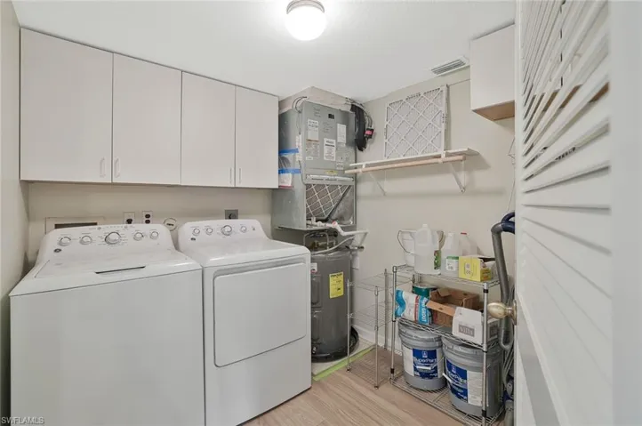Laundry room with washing machine and dryer, light wood finished floors, cabinet space, and heating unit