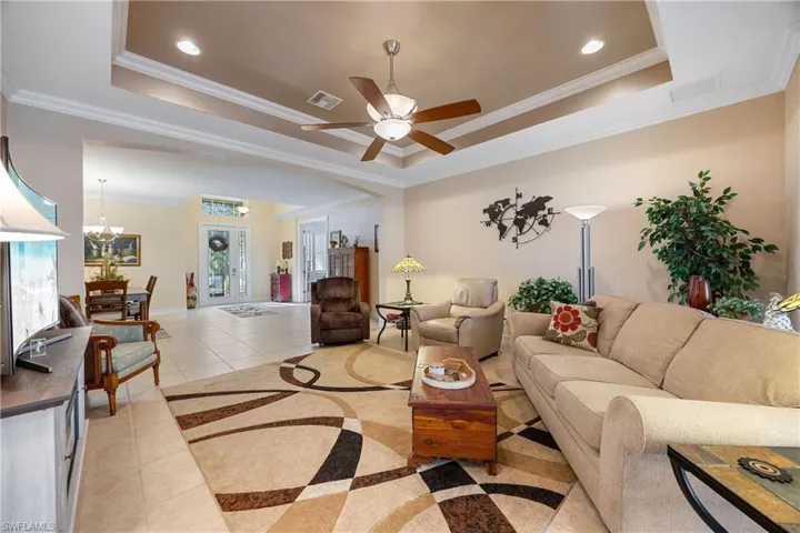 Tiled living room with a raised ceiling, crown molding, and ceiling fan with notable chandelier