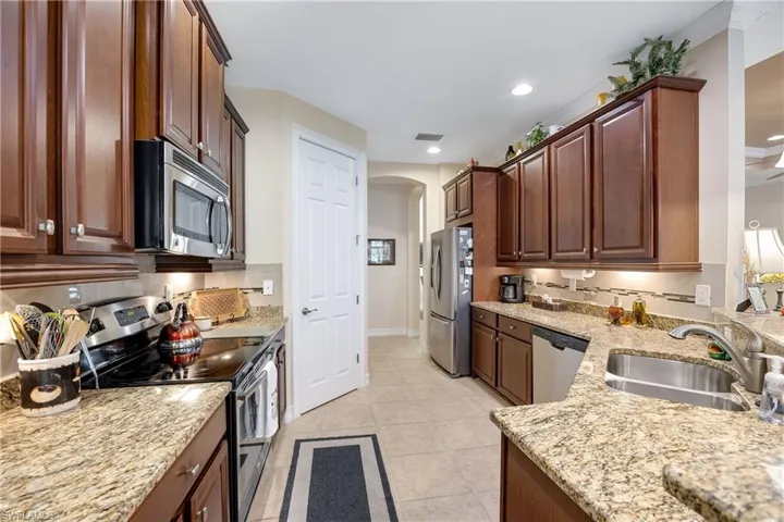 Kitchen featuring light stone countertops, sink, crown molding, light tile patterned floors, and appliances with stainless steel finishes
