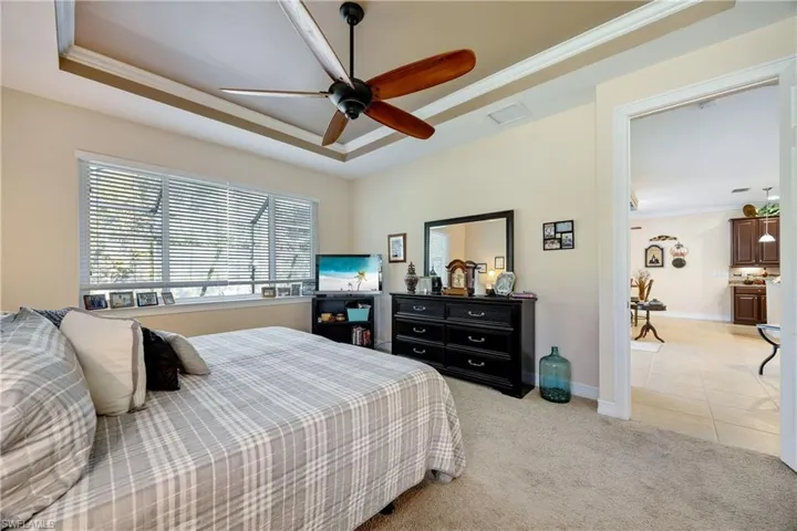 Carpeted bedroom with ceiling fan, ornamental molding, and a tray ceiling