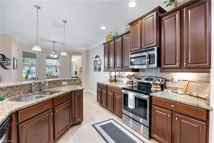 Kitchen featuring hanging light fixtures, light tile patterned floors, ornamental molding, appliances with stainless steel finishes, and light stone counters