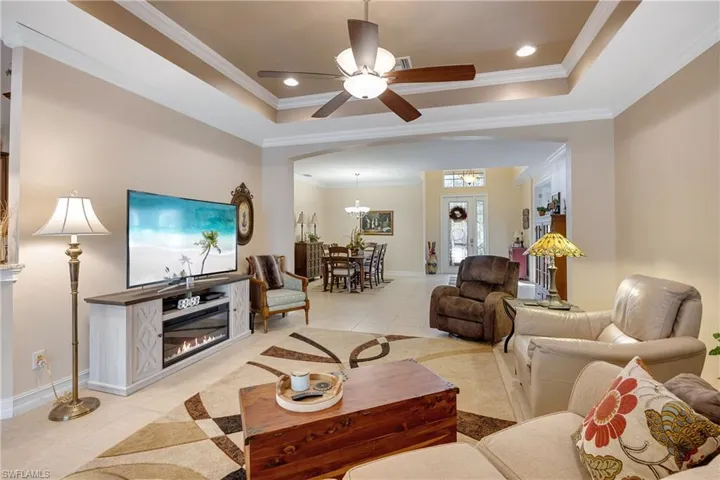 Living room with a raised ceiling, crown molding, light tile patterned flooring, and ceiling fan