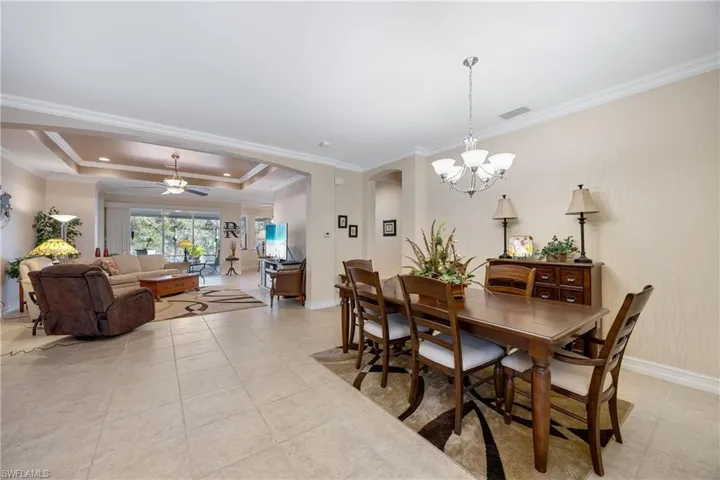 Tiled dining space with ceiling fan with notable chandelier, a raised ceiling, and crown molding