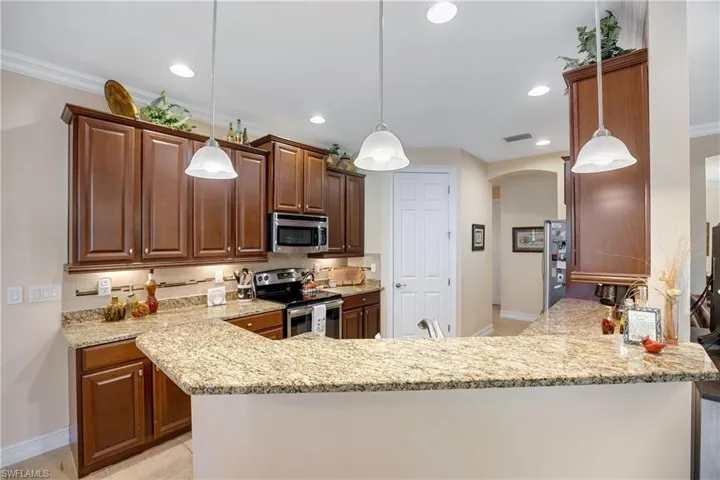 Kitchen with kitchen peninsula, light stone countertops, stainless steel appliances, and hanging light fixtures