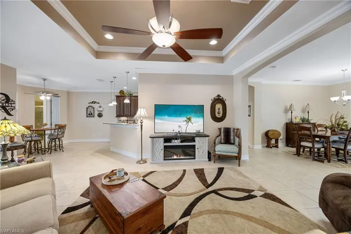 Tiled living room with ceiling fan with notable chandelier and ornamental molding