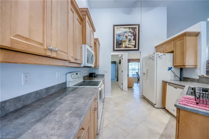 Kitchen with white appliances, light tile patterned floors, light brown cabinets, and a towering ceiling
