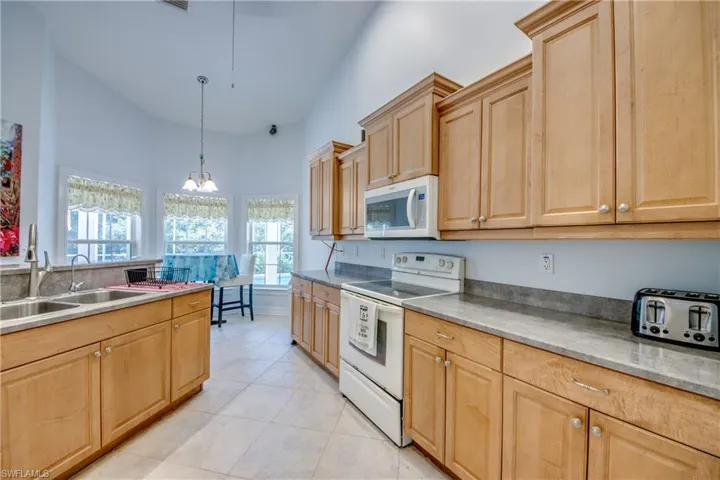 Kitchen featuring white appliances, light brown cabinets, light tile patterned floors, a chandelier, and pendant lighting
