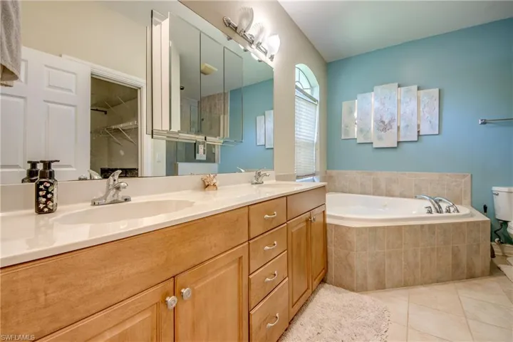 Full bath with double vanity, tile patterned floors, a garden tub, and a spacious closet